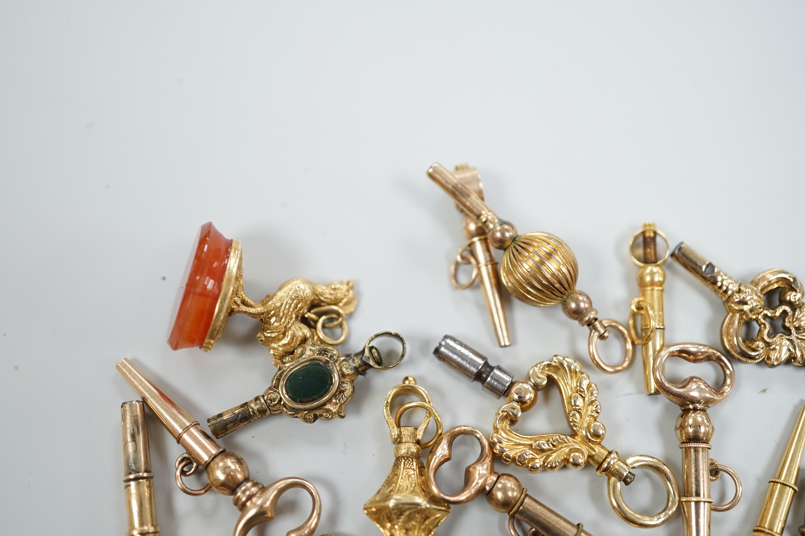 Twenty assorted mainly 19th century yellow metal small watch keys, including trade insignia, bloodstone set and keys to be turned in one direction, largest 37mm, together with a 19th century yellow metal overlaid and aga